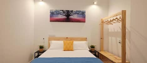 A bedroom with a bed, a nightstand, a bedside table, a wooden wardrobe, and a wall-mounted painting.