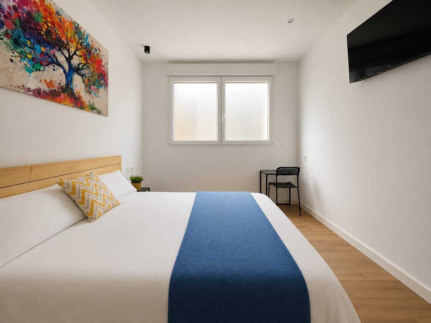 A bedroom with a bed, a chair, a TV, and a window.