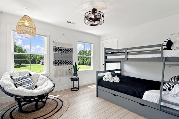 A modern bedroom with a bunk bed, a rattan chair, and a large window offering a view of the outdoors.