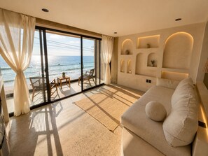A spacious room with a large sliding glass door leading to a balcony overlooking the ocean. Inside, there is a comfortable sofa with cushions and a small table with chairs. - Luxury Beachfront with King Bed & AC (Tijuana)