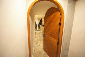 A hallway with a wooden door, a tiled floor, and a view into a room with a bed and curtains. - Luxury Beachfront with King Bed & AC (Tijuana)