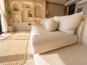 A modern living room with a beige sofa, a woven rug, and built-in shelving with decorative items. - Luxury Beachfront with King Bed & AC (Tijuana)