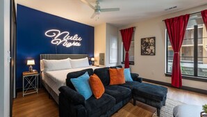 Una camera d'albergo con un letto, un divano, una ventola a soffitto e una parete con insegna luminosa al neon.