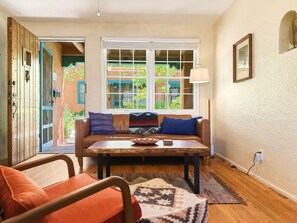 A cozy living room with a sofa, coffee table, and a view of a courtyard. - Casa de las Flores (Santa Fe)