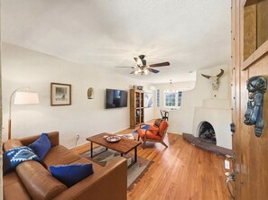 A living room with a brown leather sofa, a wooden coffee table, a television, and a fireplace. - Casa de las Flores (Santa Fe)