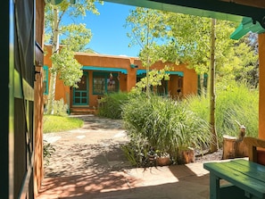 A pathway leading to a building with a green door and windows, surrounded by greenery and a wooden bench. - Casa de las Flores (Santa Fe)