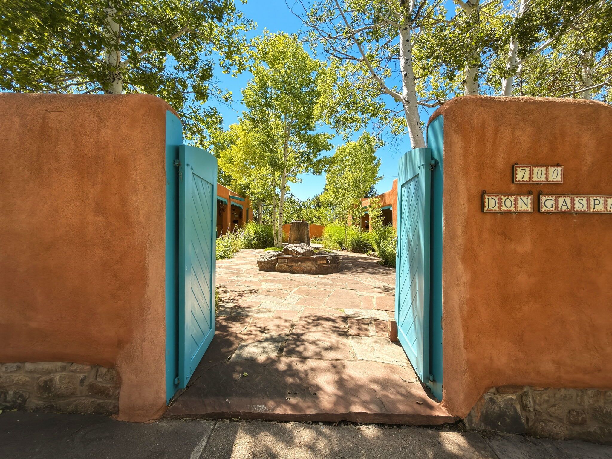 A courtyard with a stone pathway leading to a building entrance, surrounded by trees and a clear sky.