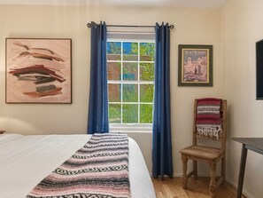 A bedroom with a bed, a window with curtains, a chair, and two framed pictures on the wall. - Casa de las Flores (Santa Fe)