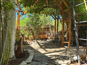 A covered outdoor area with stone flooring, wooden pergola, and seating arrangements. - Casa de las Flores (Santa Fe)