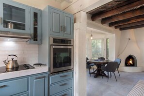 A kitchen with blue cabinets, a stove, and an oven. There is a dining area with a table and chairs. A fireplace is visible in the background. - Sunset Mountain Casita - 1 Bedroom (Santa Fe)