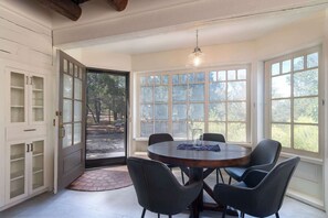 A dining area with a round table, four chairs, a hanging light fixture, and large windows with a view of trees. - Sunset Mountain Casita - 1 Bedroom (Santa Fe)