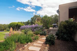 A garden pathway leading to a building entrance, surrounded by various plants and a clear sky. - Sunset Mountain Casita - 1 Bedroom (Santa Fe)