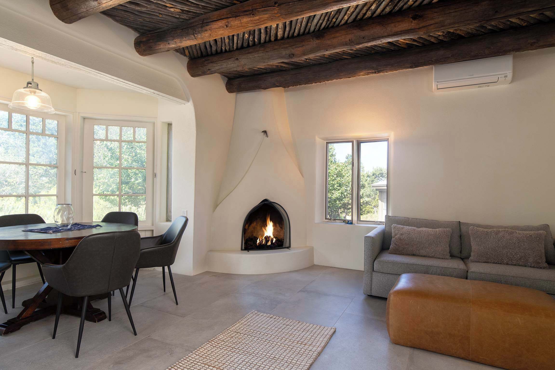 A room with a fireplace, a dining table with chairs, a sofa, and a window.