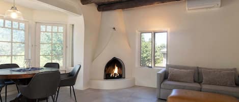 A room with a fireplace, a dining table with chairs, a sofa, and a window.