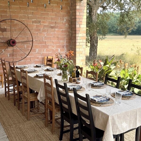 Un espace de restauration en plein air avec un mur en briques, des chaises en bois, une table dressée avec des assiettes, des verres et un vase de fleurs.