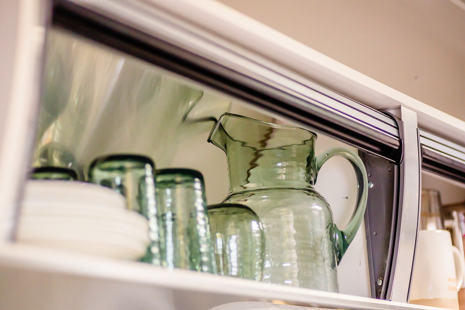 A kitchen cabinet with glassware, including a pitcher and several bottles.