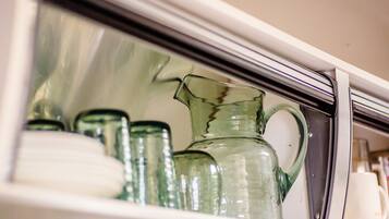 A kitchen cabinet with glassware, including a pitcher and several bottles.