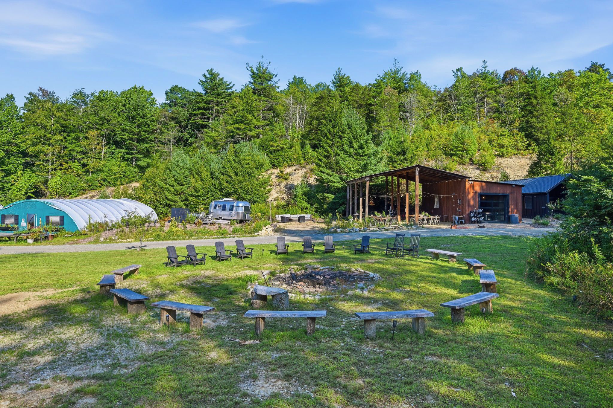 A campsite with a fire pit, picnic tables, and a covered area with seating.