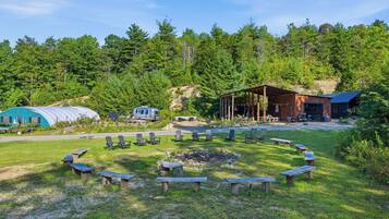 A campsite with a fire pit, picnic tables, and a covered area with seating.