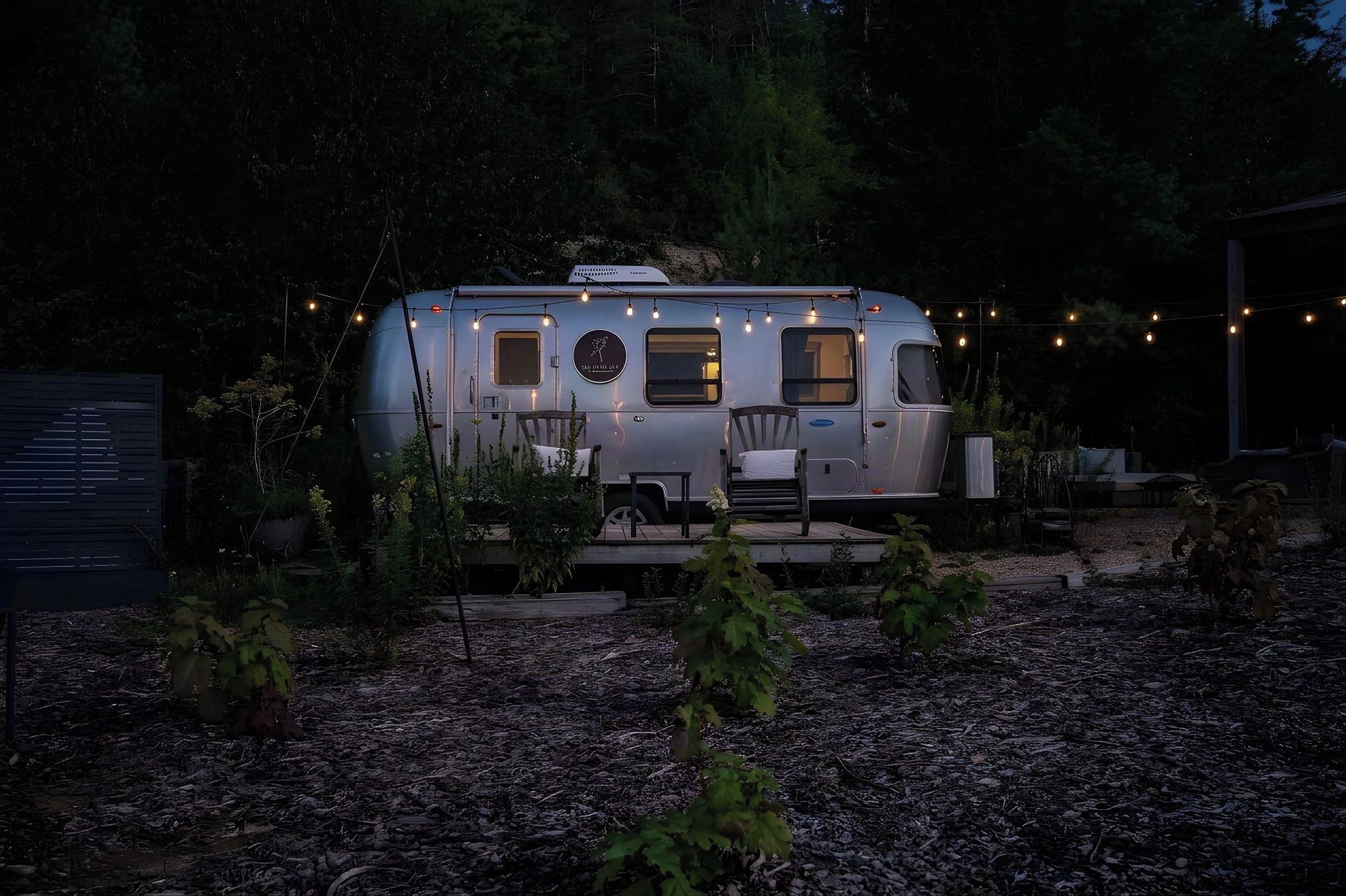 A stationary RV with a dining area and a small porch, surrounded by trees and string lights.