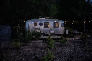 A stationary RV with a dining area and a small porch, surrounded by trees and string lights.