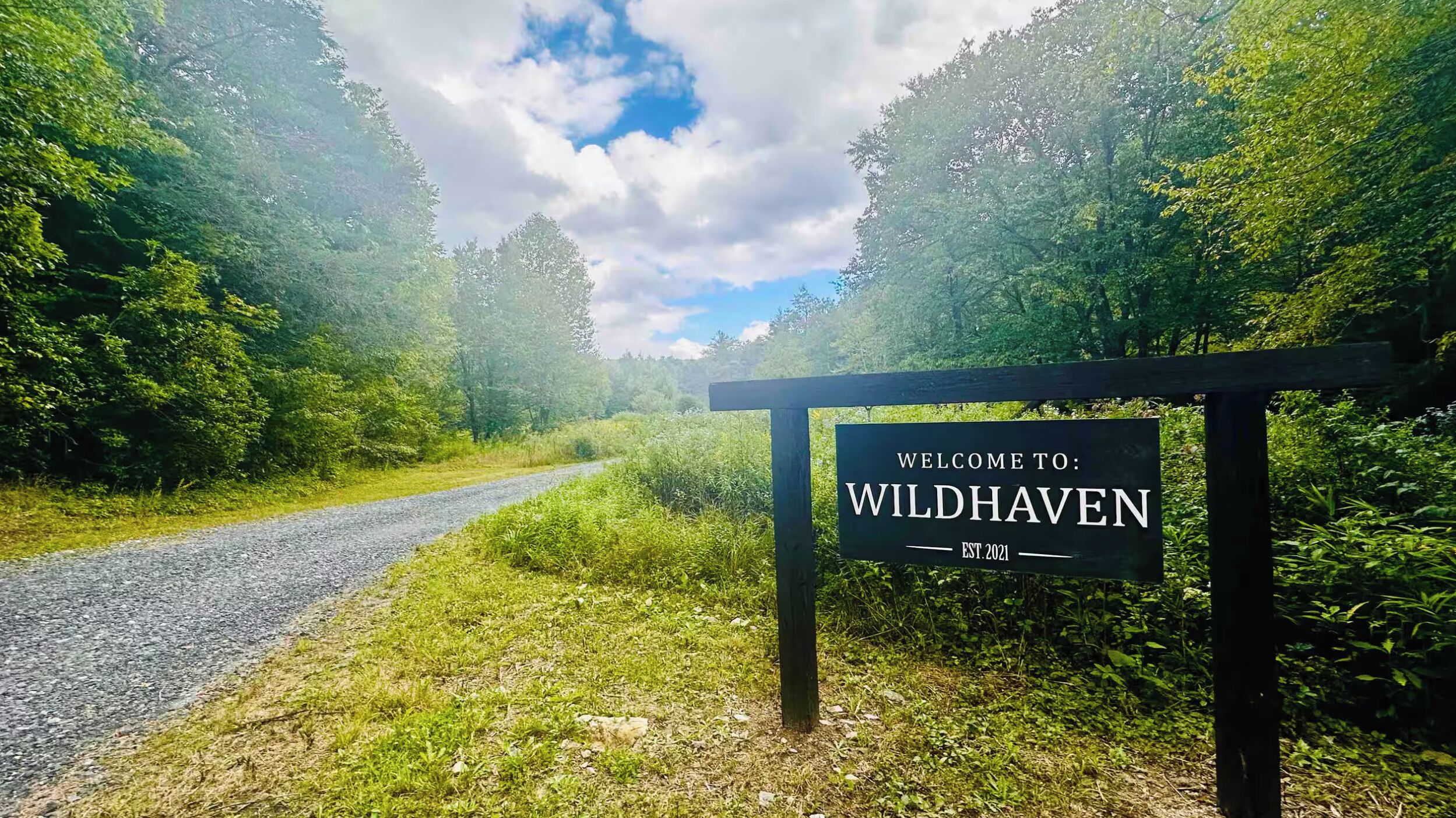 Schild mit dem Schriftzug Wildhaven, eine Schotterstraße und dichter Wald.