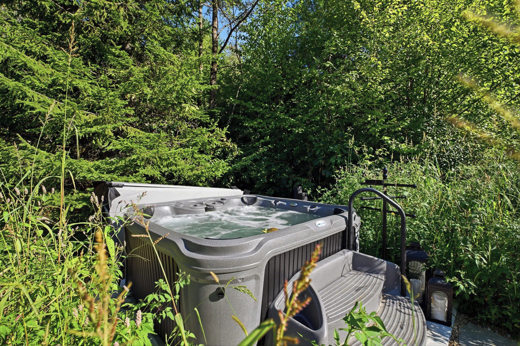 Un jacuzzi rodeado de abundante vegetación y una terraza de madera.