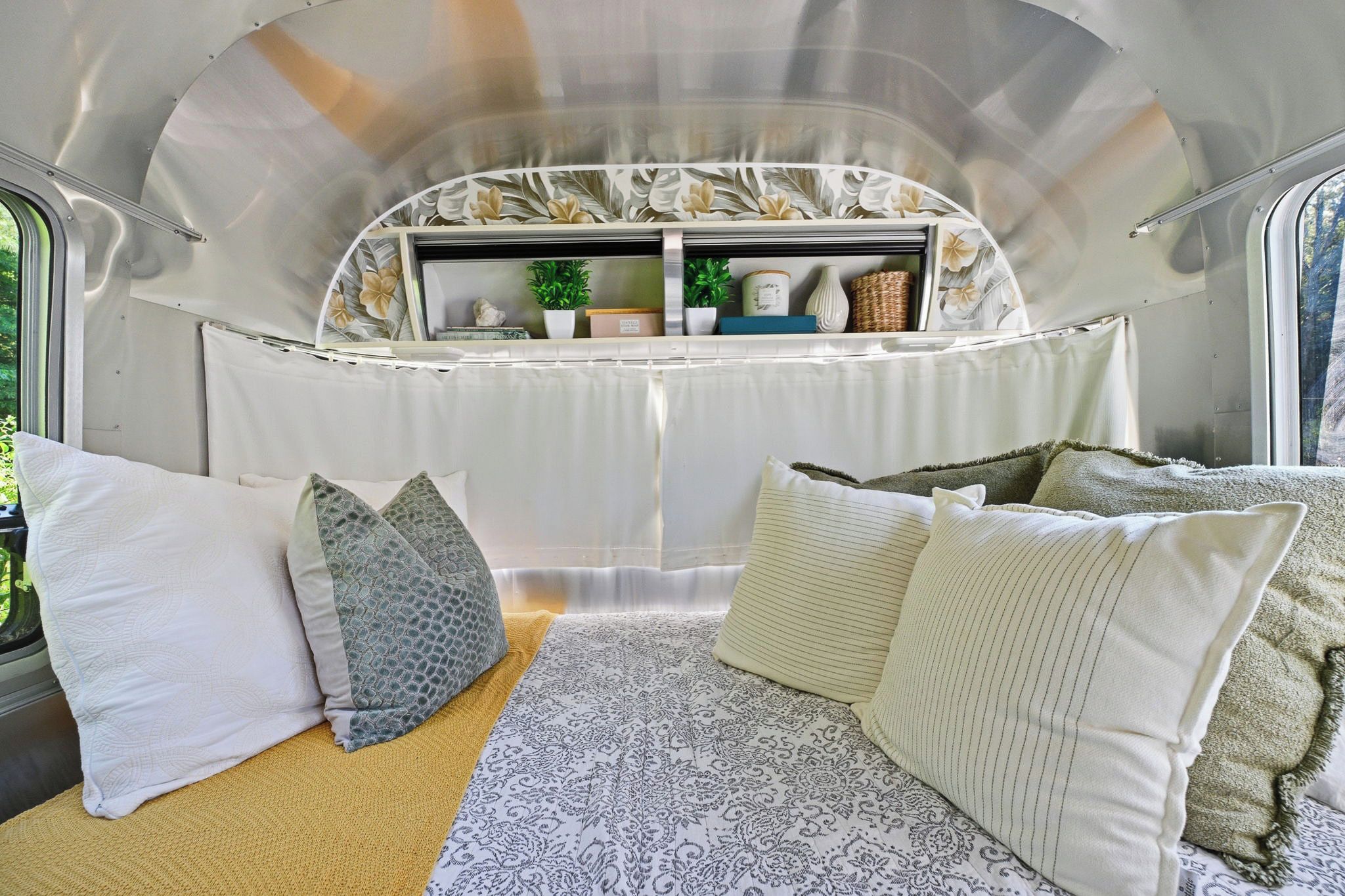 A cozy interior with a bed, pillows, a window, and a shelf with decorative items.