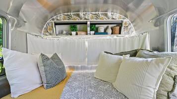A cozy interior with a bed, pillows, a window, and a shelf with decorative items.