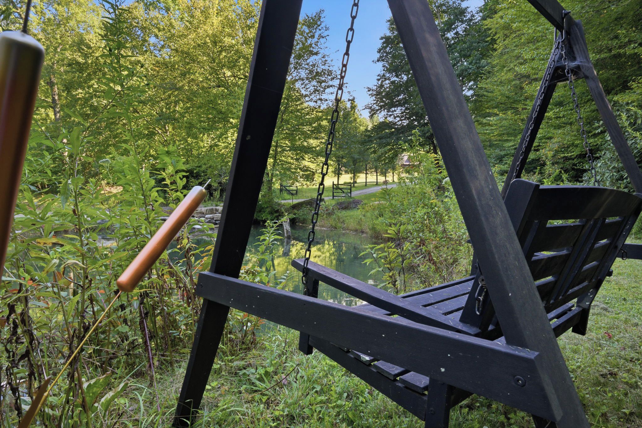 A wooden swing set in a natural setting with a pond and trees in the background.