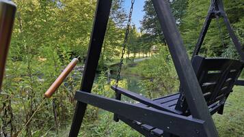 A wooden swing set in a natural setting with a pond and trees in the background.