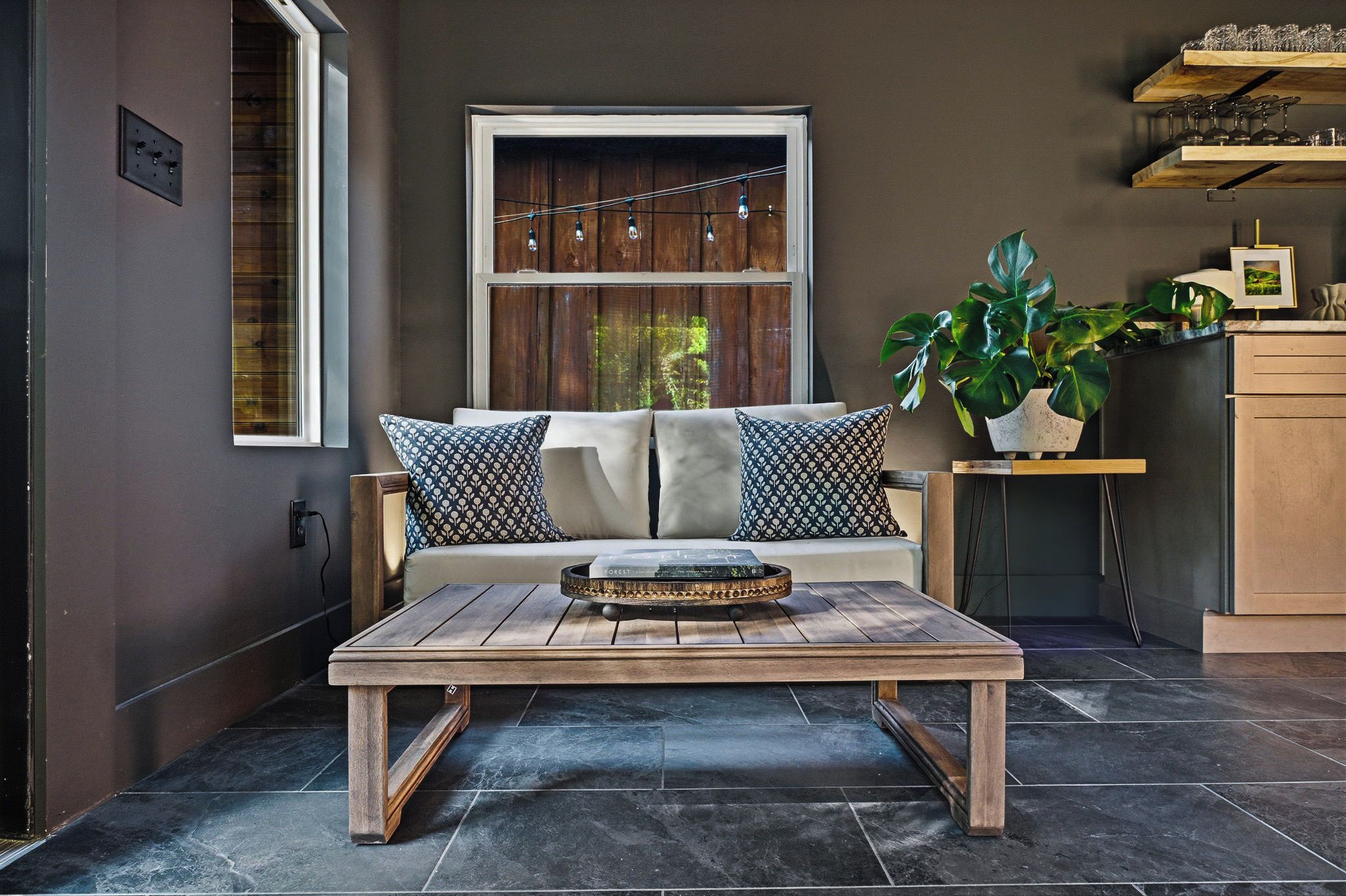 Una sala de estar moderna con una mesa de centro de madera, un sofá con cojines estampados, una planta en maceta y una ventana con cortinas.