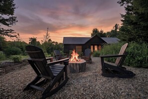 A fire pit with chairs around it, a building in the background, and a gravel ground.