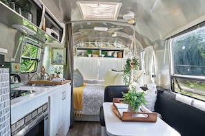 A compact RV interior with a kitchenette, a dining area, and a sleeping berth. - Petite Airstream Cottage w/Private Hot Tub + Sauna Access by Blue Ridge Parkway (Newland)