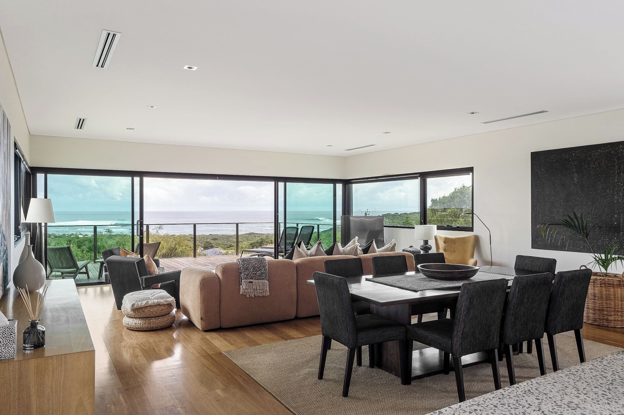 A modern living room with a large window overlooking a scenic view, a dining area with a table and chairs, and a cozy seating area with a sofa and cushions.
