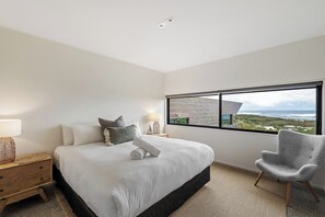 Un dormitorio con una cama grande, vistas al océano y una silla moderna.