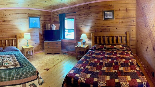 A cabin-style room with two beds, wooden walls, a television, and a dresser. - Log Cabin 2-bedroom lake view 20 minutes to Branson (Forsyth)