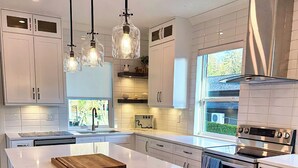 Uma cozinha moderna com uma ilha grande, luminárias pendentes e eletrodomésticos de aço inoxidável.