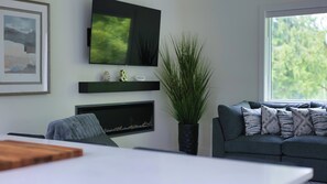 Ein Wohnzimmer mit Flachbildfernseher, Kamin, Sofa und einem großen Fenster.