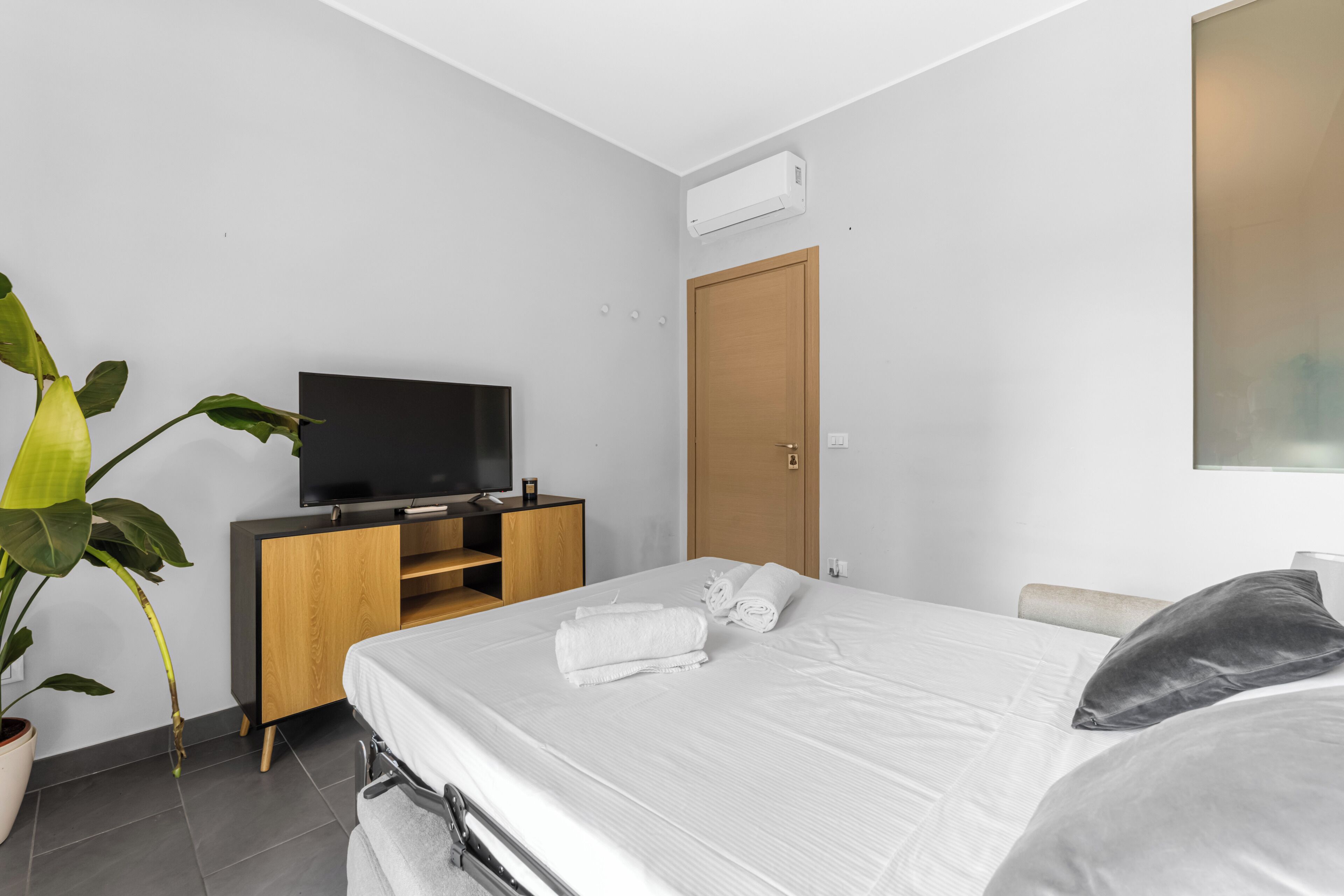 Ein modernes Hotelzimmer mit einem Bett, einem Fernseher auf einem Holztisch, einer Tür und einer Topfpflanze.
