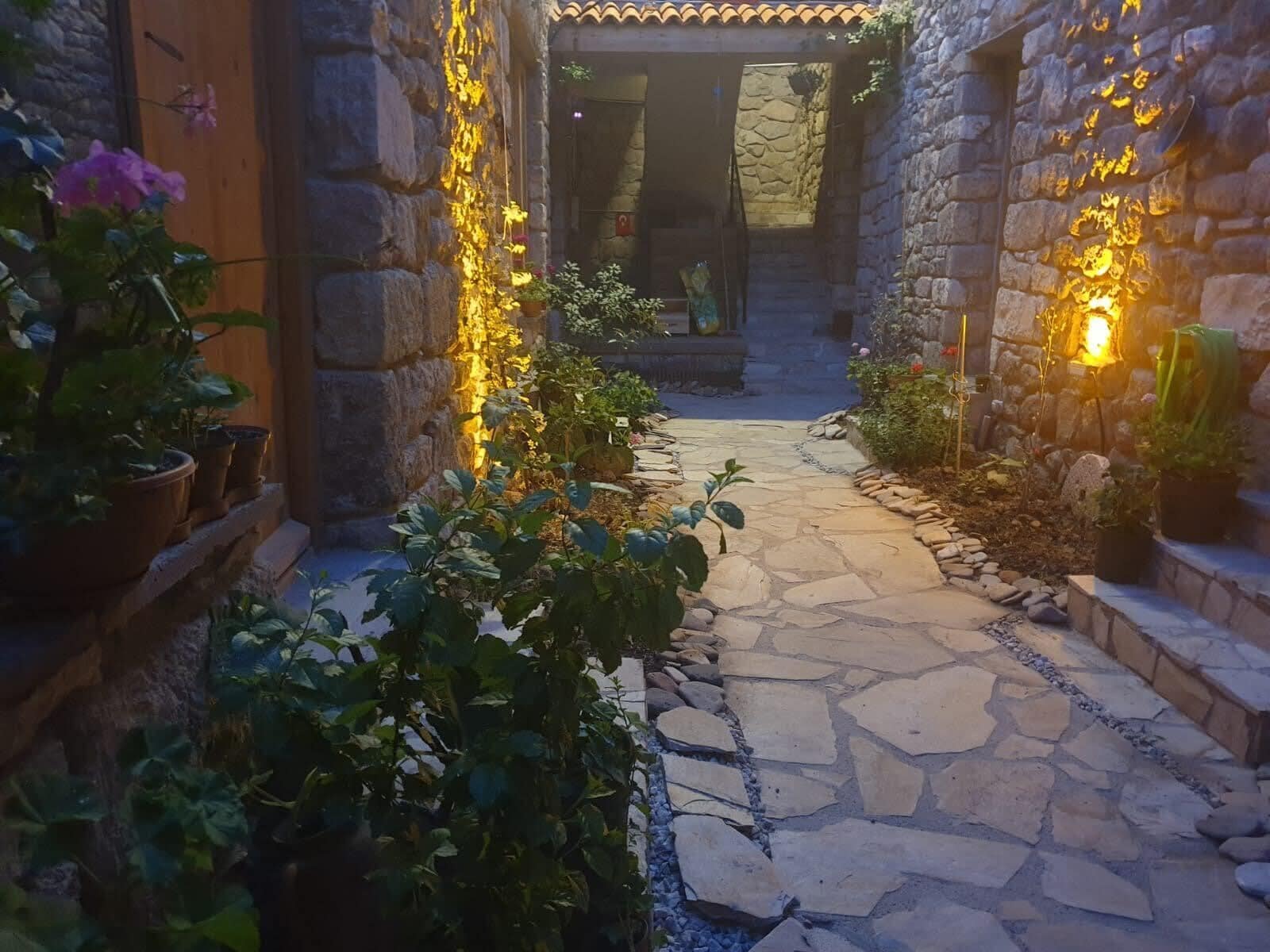 A stone pathway leading to a building entrance, surrounded by potted plants and stone walls.