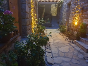 Un camino de piedra que lleva a la entrada de un edificio, rodeado de macetas con plantas y muros de piedra.