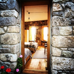 Una habitación con paredes de piedra, una cama, una silla de madera y un ventanal.