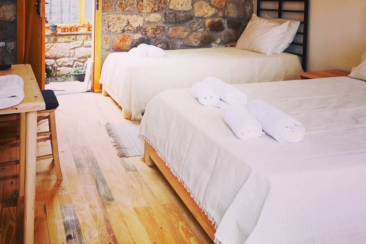 Una habitación con dos camas, una mesa de madera y una pared de piedra.