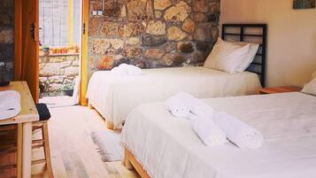 A room with two beds, a wooden table, and a stone wall.
