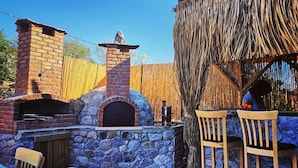 Une terrasse extérieure dotée d’un four en briques, de murs en pierre et de mobilier en bois.