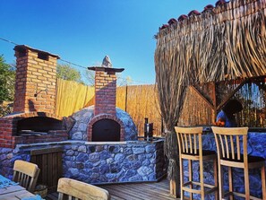 Un patio al aire libre con un horno de ladrillo, paredes de piedra y mobiliario de madera.