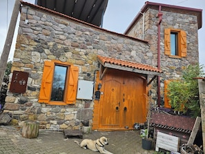 A stone building with a wooden door and shutters, a mailbox, and a dog lying on the ground. - Teora butik otel (Ayvacik)