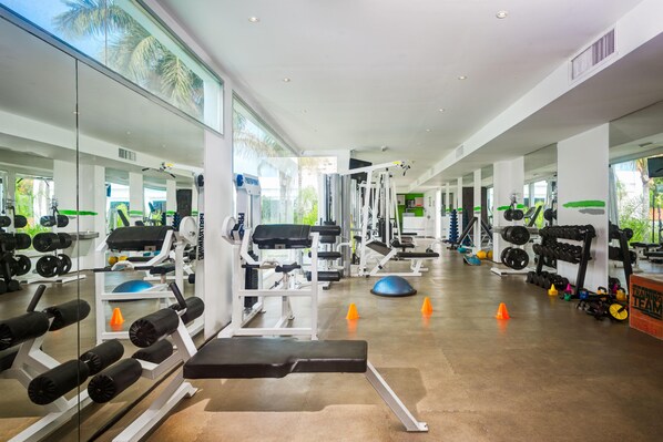 A modern gym with various exercise equipment, mirrors, and a clear view of the outdoors. - Hotel Kristoff (Maracaibo)