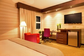 A hotel room with a bed, desk, chair, TV, and a small refrigerator. - Hotel Kristoff (Maracaibo)